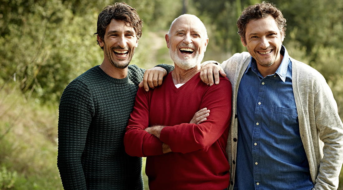 Portrait of cheerful senior man standing with sons at park